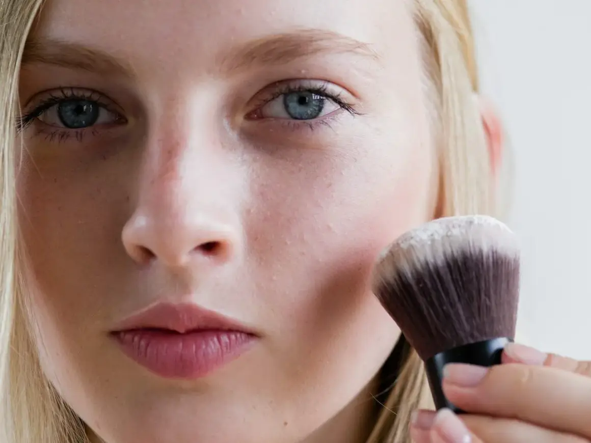 Blondynka nakłada puder transparentny pędzlem. To sekret naturalnego wykończenia makijażu.