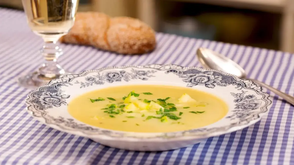 Eine cremige Zucchini-Suppe mit frischer Petersilie in einer eleganten Schüssel, daneben ein Glas Weißwein und ein Brot.