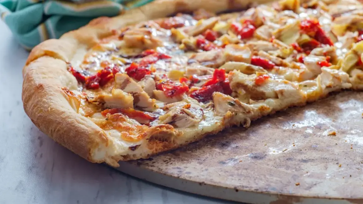 Pyszna pizza włoska z kurczakiem i suszonymi pomidorami, z chrupiącym brzegiem, na kamieniu do pieczenia.