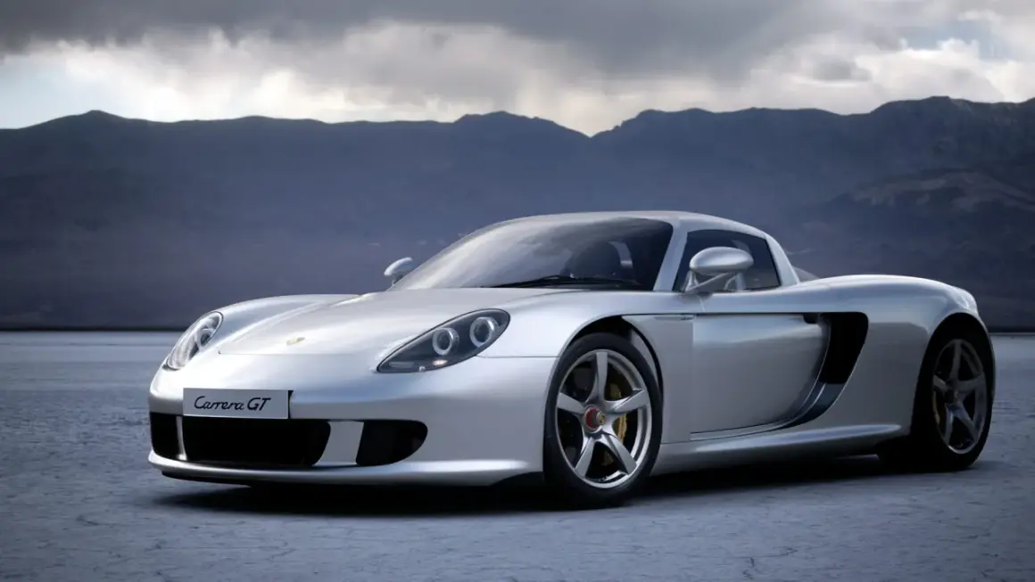 Srebrny Porsche Carrera GT na pustkowiu, z górami w tle.