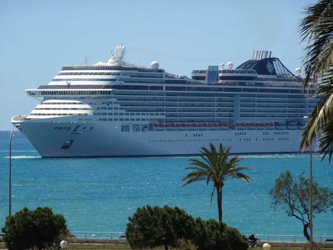 Ogromny statek wycieczkowy MSC Divina płynie po turkusowym morzu, z palmami i zielenią na pierwszym planie.