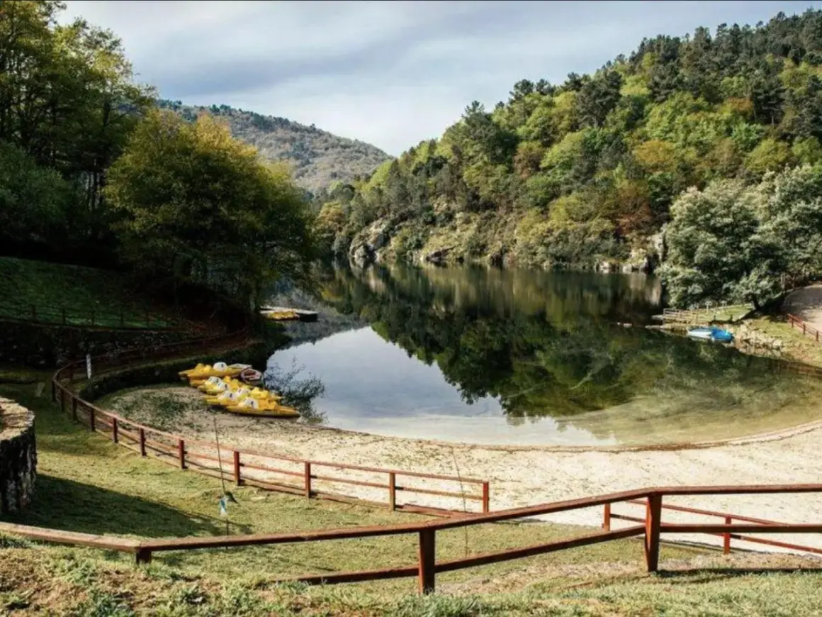 Playa fluvial a Calzada con kayaks amarillos esperando en la arena, rodeada de árboles verdes y un río tranquilo.