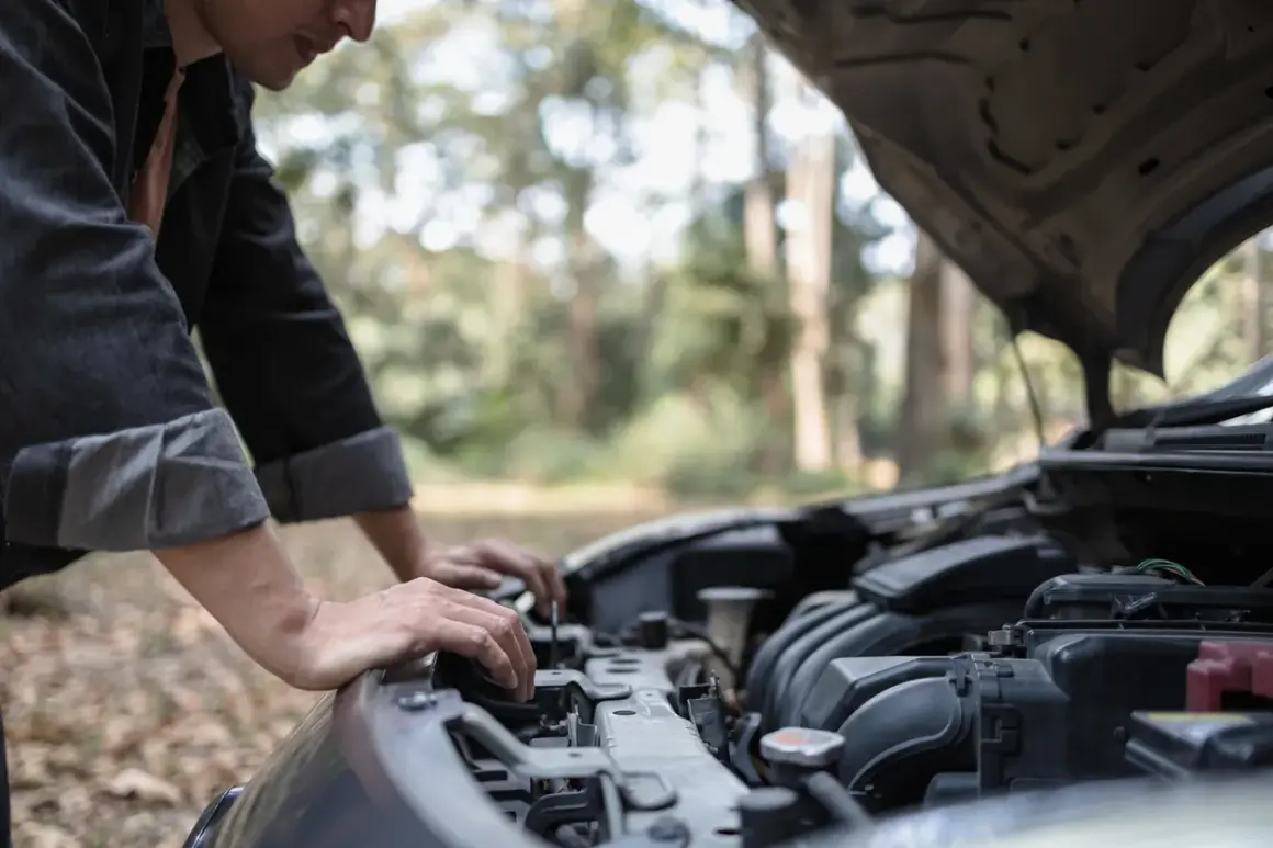 Un homme regarde le moteur de sa voiture qui cale à bas régime, bloqué en pleine nature.
