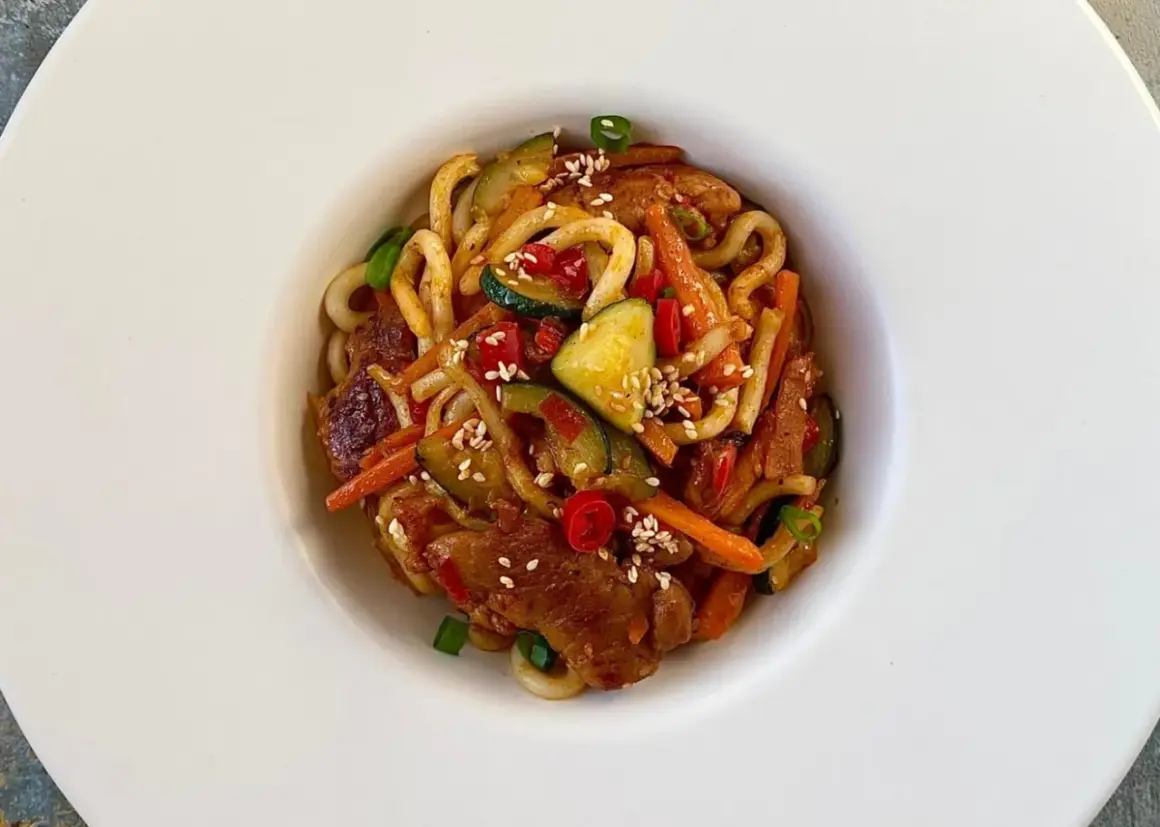 Szybki i tani obiad: makaron udon z kurczakiem, cukinią, marchewką i papryką, posypany sezamem.
