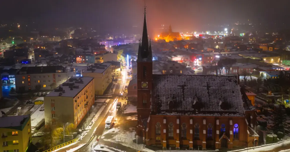 Nocna panorama Kościerzyny, ośnieżona trasa miejska z kościołem w centrum i rozświetlonymi budynkami.