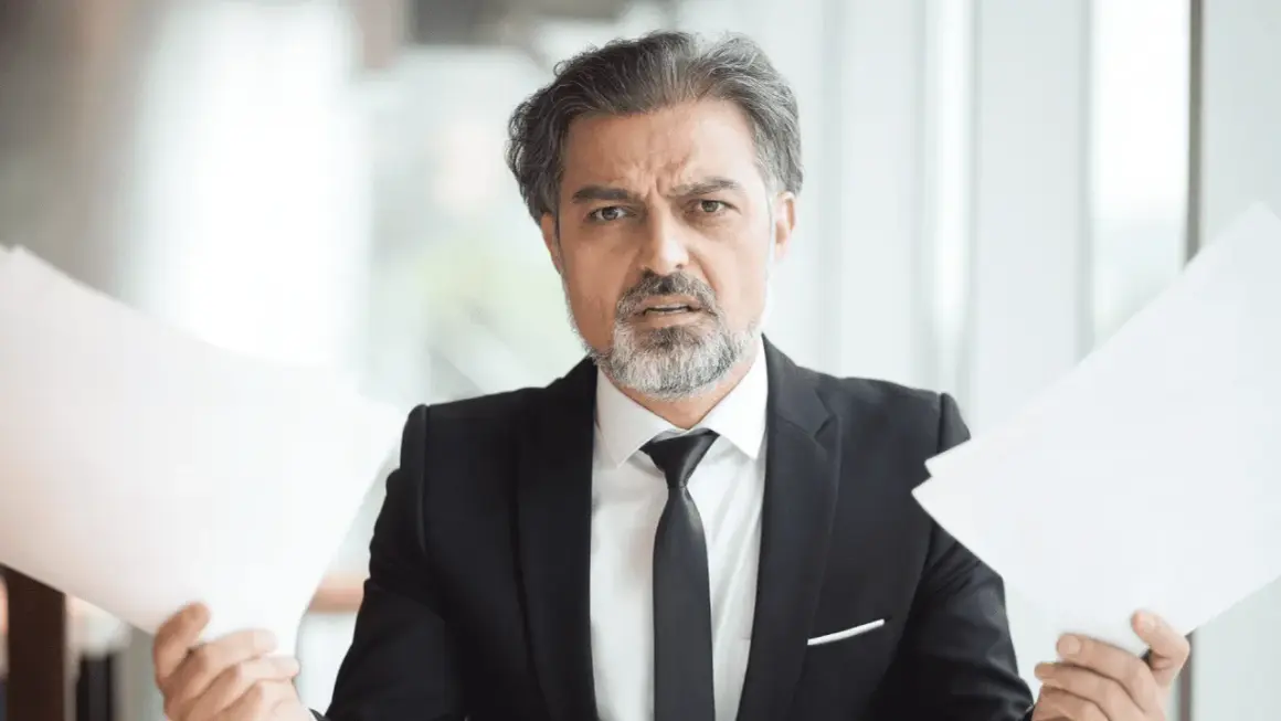Hombre con traje y papeles, preocupado por cuanto cobra una inmobiliaria por alquilar un piso.