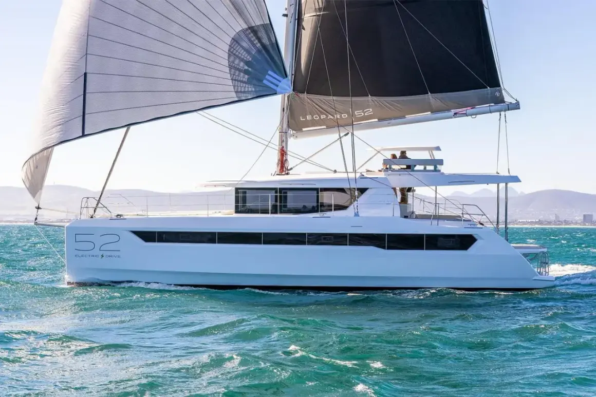 Un catamarano Leopard 52 con vele spiegate naviga su acque turchesi, con montagne sullo sfondo.