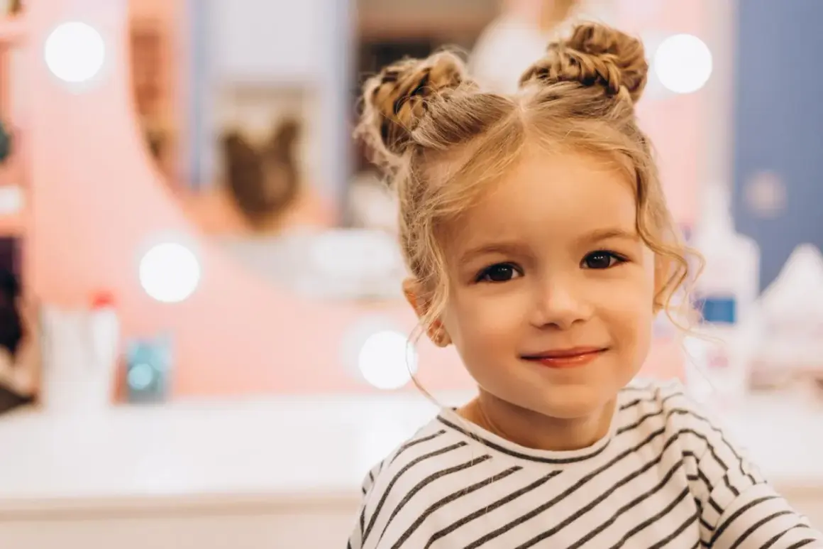 Urocza dziewczynka z blond włosami upiętymi w dwa kucyki. Jej fryzura to idealne włosy dla dziewczyn, które chcą wyglądać modnie i dziewczęco.