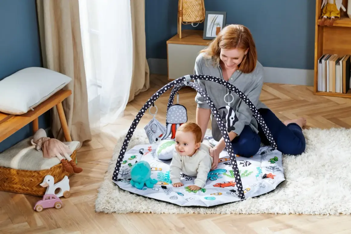 Mama bawi się z dzieckiem na macie edukacyjnej z motywem podwodnym. Idealna mata dla niemowlaka do rozwoju.