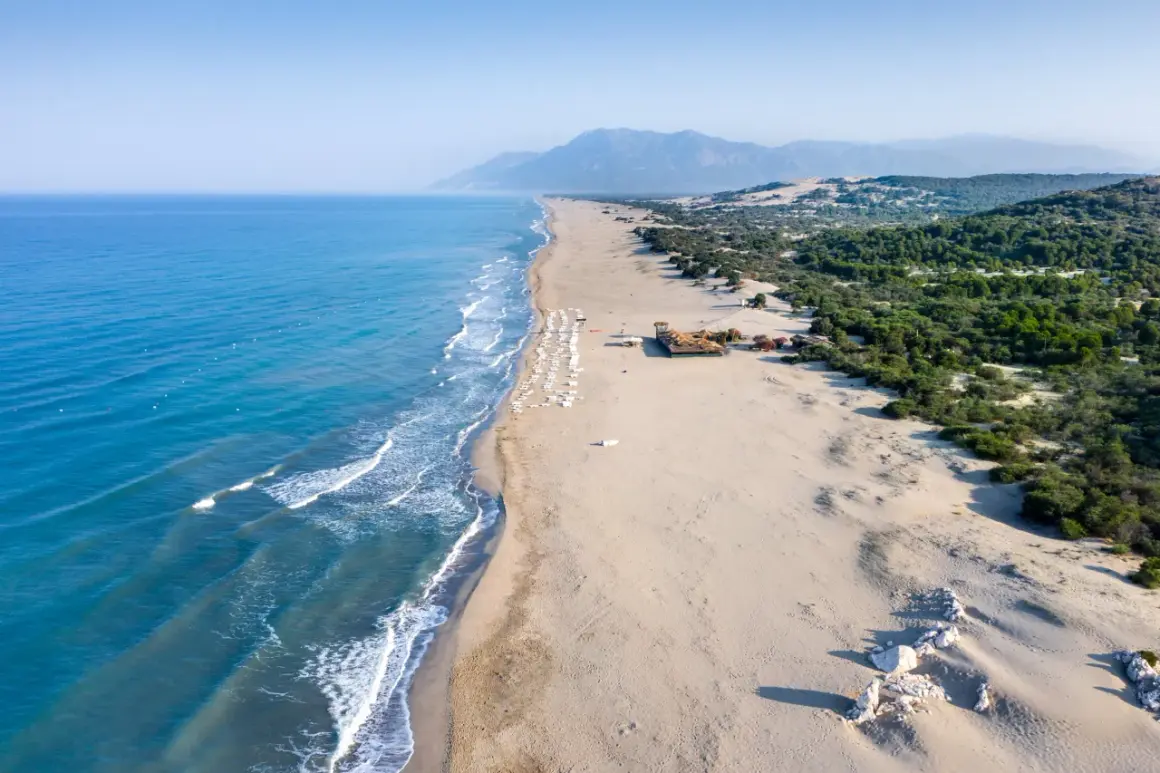 Piękne turcja plaże z turkusową wodą, piaszczystym brzegiem i zielonymi wzgórzami w tle. Rząd leżaków zaprasza do odpoczynku.