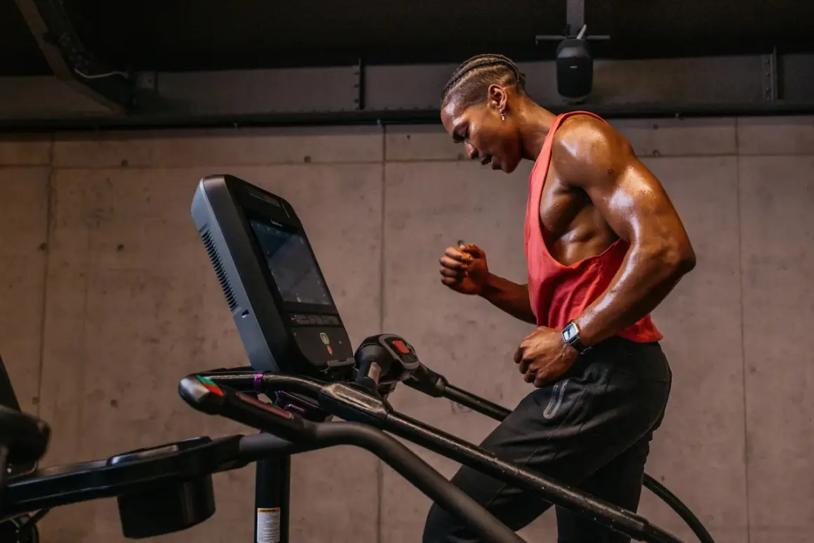 Schweißglänzender Mann im roten Tanktop gibt alles beim liss cardio auf dem Laufband.