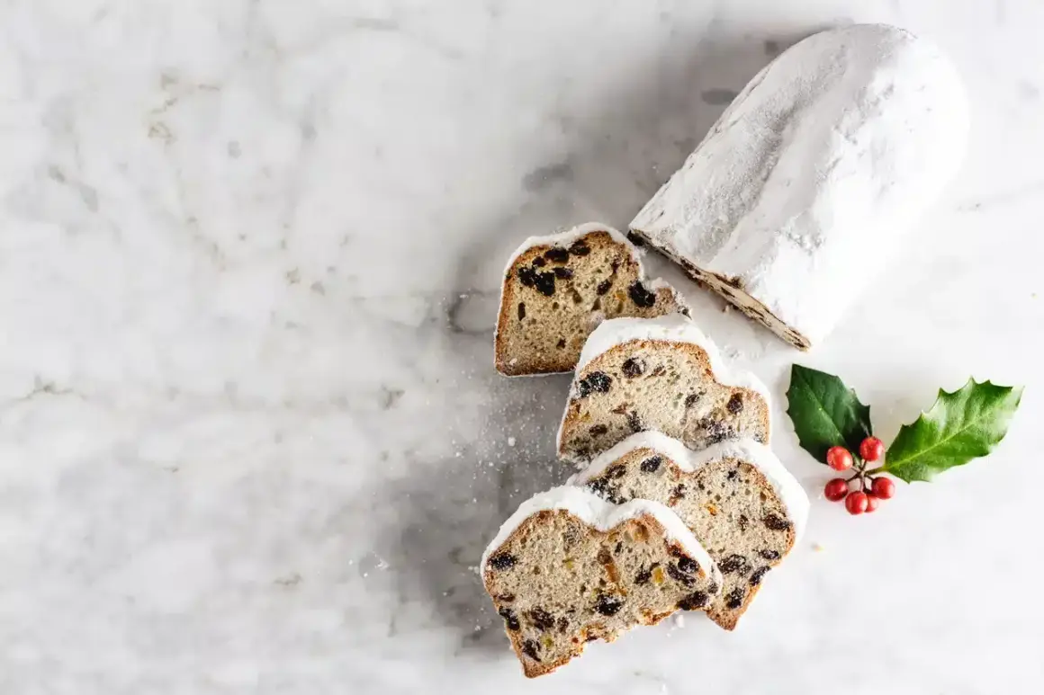 Le stollen, un délice de Noël, est saupoudré de sucre glace. Des tranches révèlent des fruits secs et des baies rouges sur une branche de houx.