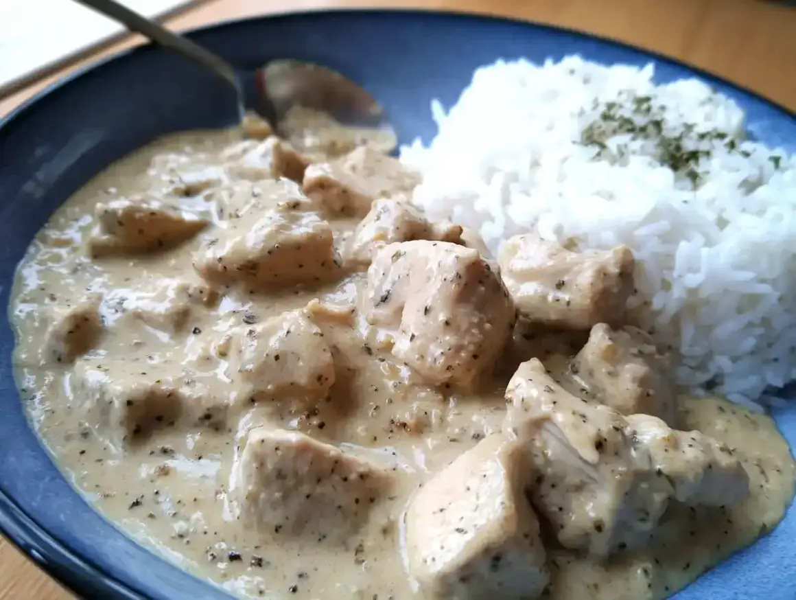 En krämig sås till kyckling och ris, med bitar av kyckling i en ljus sås. Riset är toppat med lite grön krydda.