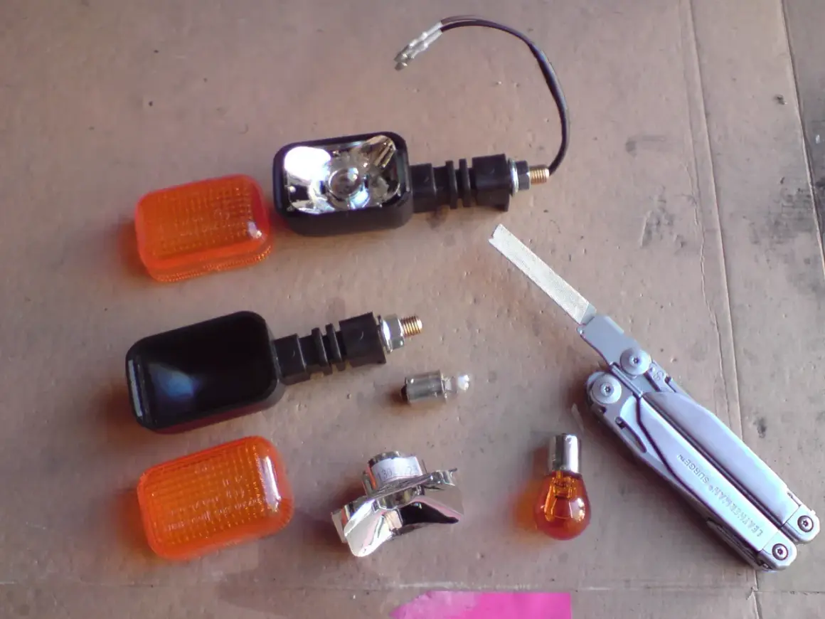 Części do wymiany żarówki kierunkowskazu motocykla: pomarańczowe klosze, obudowy, żarówki, multitool Leatherman Surge.