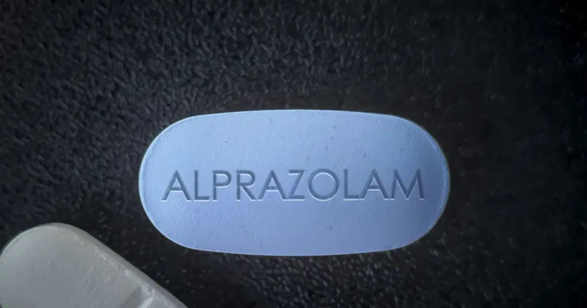 Niebieska tabletka z napisem ALPROZOLAM leży obok białej.