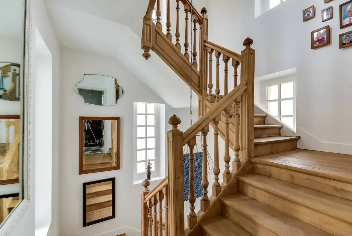 Un bel escalier en bois, prêt à être nettoyé. Des miroirs et des cadres photo décorent le mur blanc.