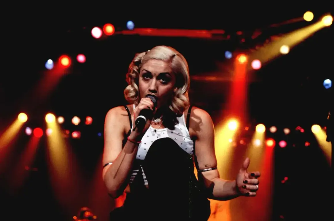 Gwen Stefani śpiewa na scenie, otoczona kolorowymi światłami.