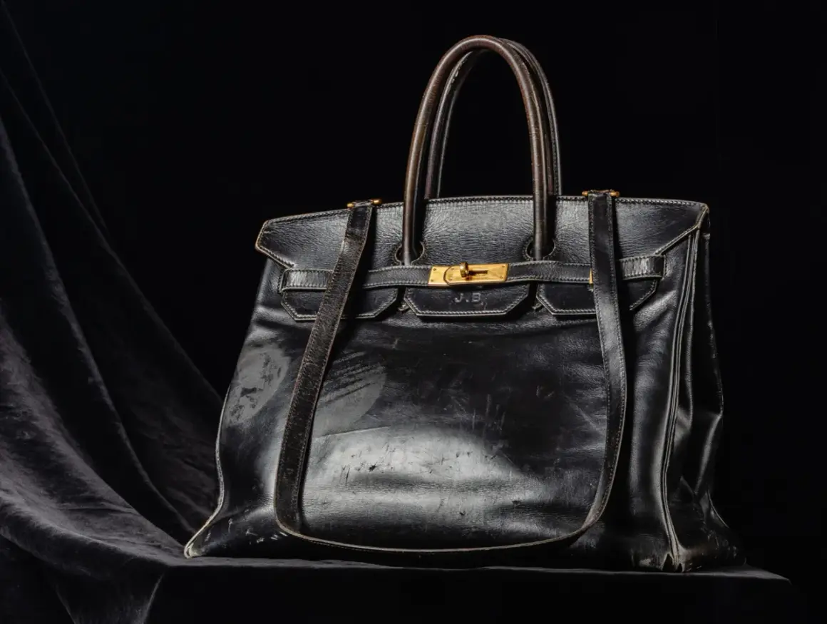 En svart, sliten läderväska i jane birkin style, med guldfärgade detaljer och initialerna J.B. präglade.