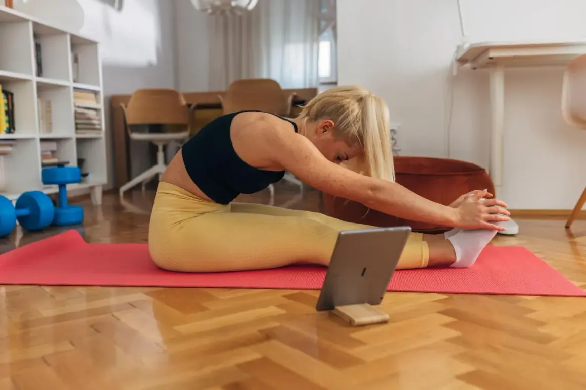 Kobieta ćwiczy w domu, sprawdzając na tablecie, czy trening siłowy spala tłuszcz. Obok leżą hantle.