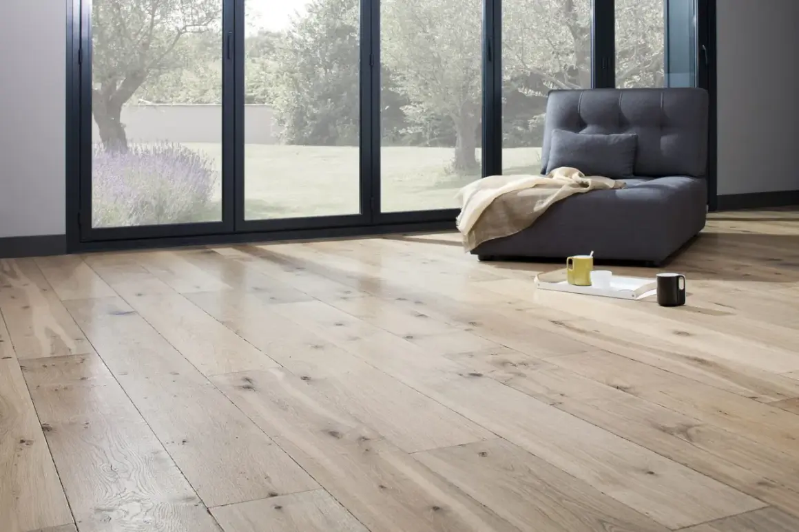 Un salon lumineux avec un parquet clair, une banquette grise et une vue sur un jardin verdoyant. Idéal pour peindre un parquet et créer une ambiance cosy.