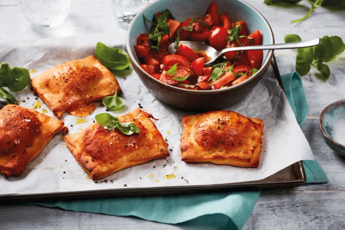 Goldbraune Teigtaschen, gefüllt und gebacken, zeigen, was man aus pizzateig machen kann. Dazu ein frischer Tomatensalat.