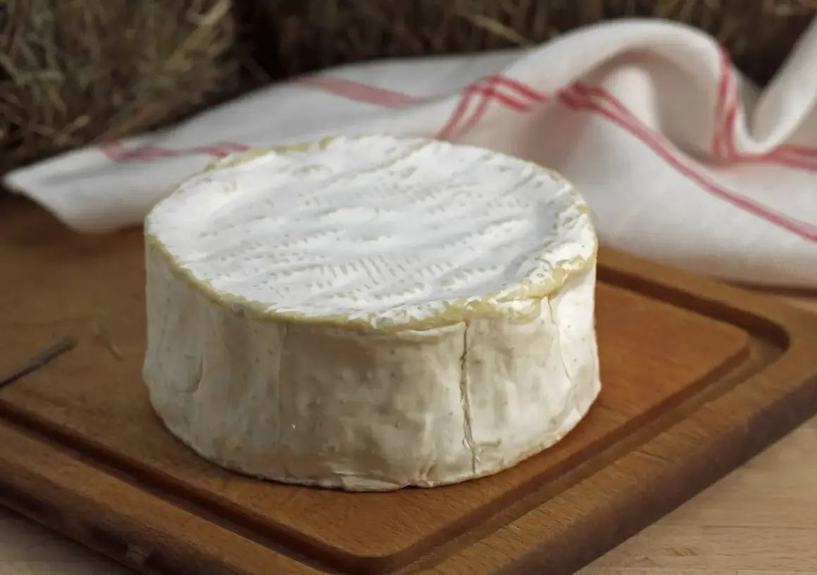 Un delicioso queso francés, con su corteza blanca y cremosa, descansa sobre una tabla de madera.