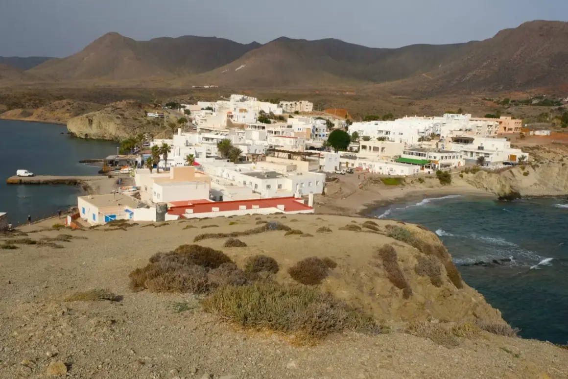 Vista panorámica de la playa Isleta del Moro, con casas blancas, mar azul y montañas áridas al fondo.