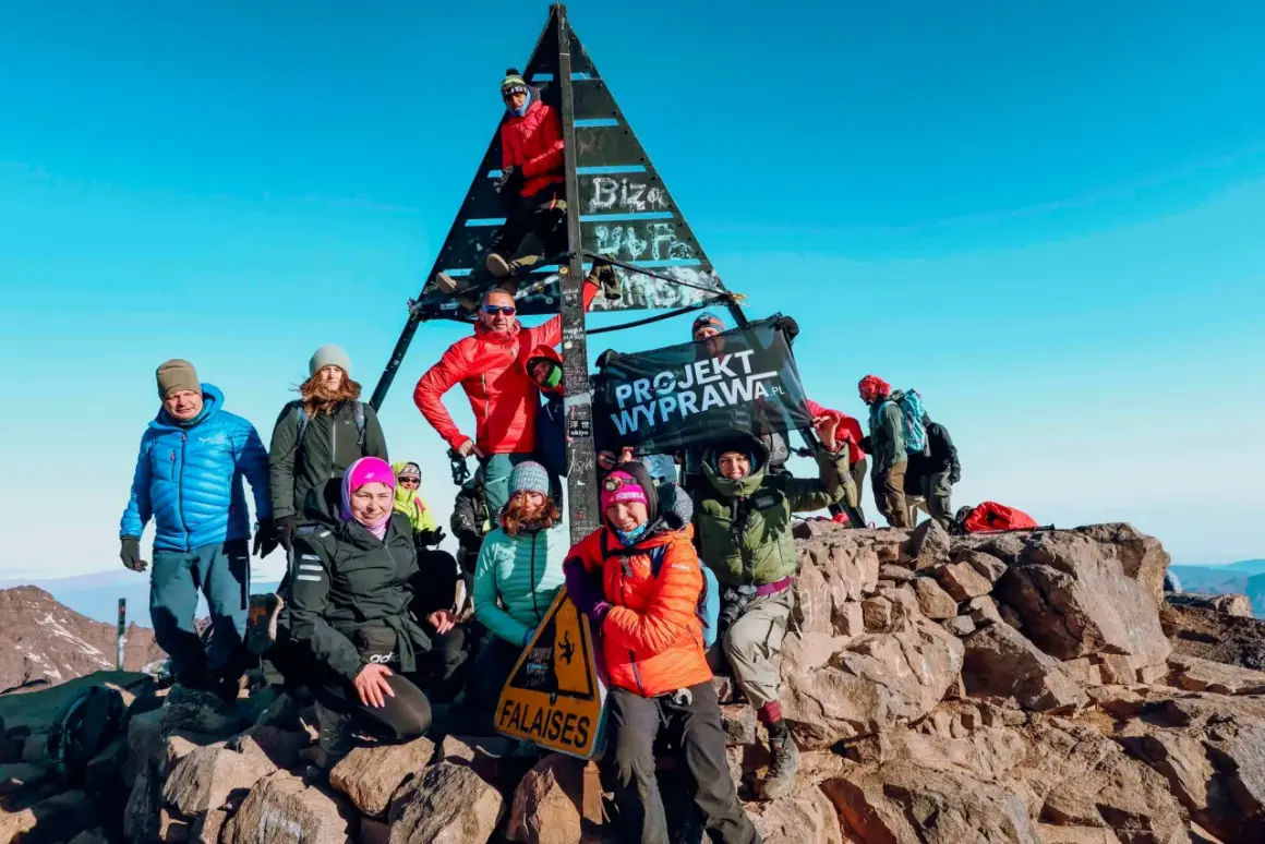 Grupa zdobywców na szczycie Jebel Toubkal podczas trekkingu. Radosna ekipa z flagą "Projekt Wyprawa.pl" cieszy się sukcesem.