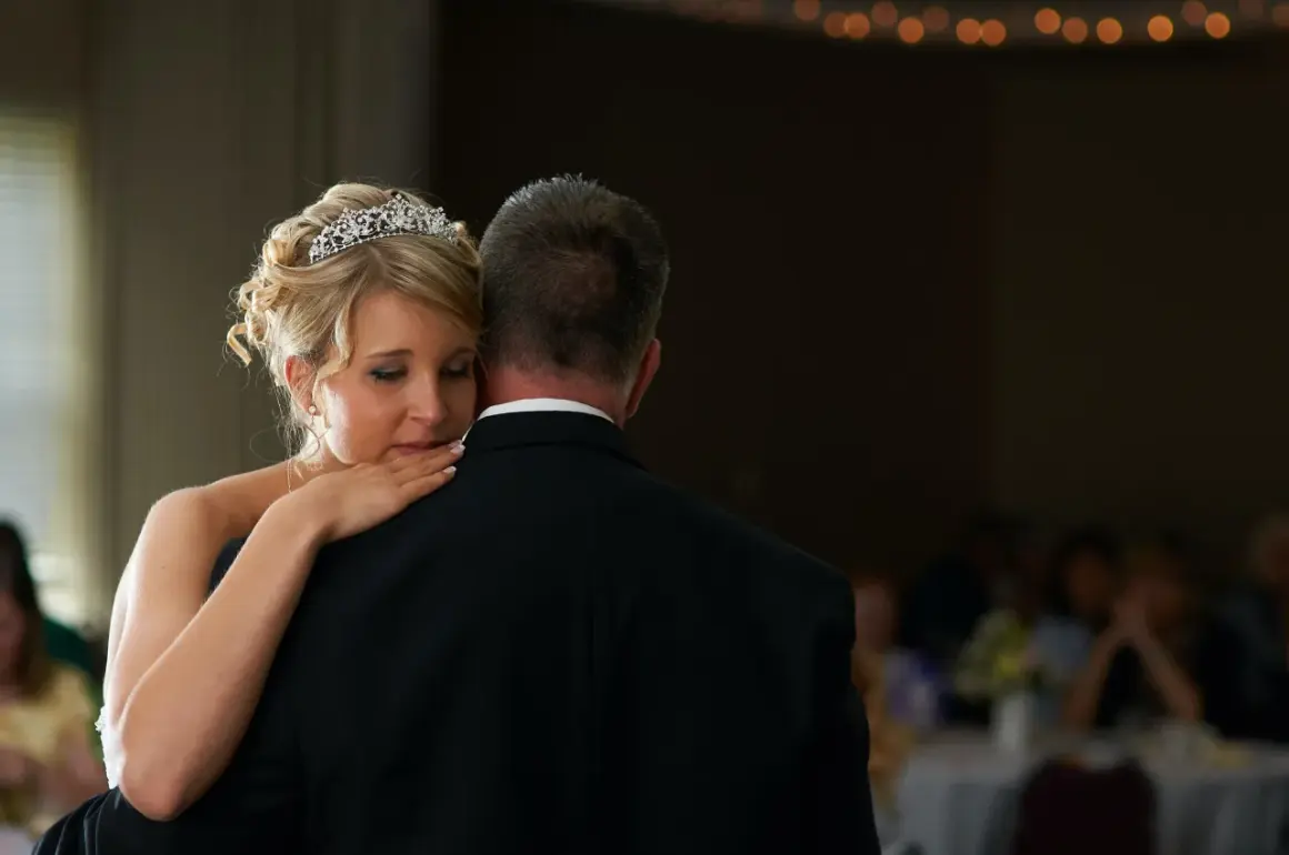 Ein zärtlicher Vater-Tochter-Tanz. Die Braut mit Diadem lehnt sich an ihren Vater, der einen schwarzen Anzug trägt.
