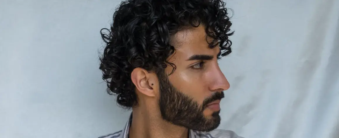 Hombre con pelo rizado oscuro y barba. Un ejemplo de como peinar pelo rizado hombre para un look natural y definido.