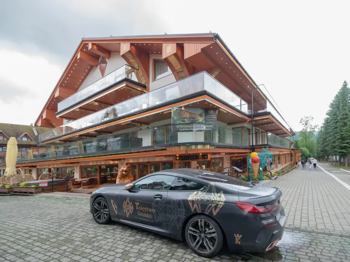 Luksusowy hotel Górski Diament z nowoczesną architekturą i przeszklonymi balkonami. Przed budynkiem stoi elegancki samochód z motywem "Księstwo Góralskie".