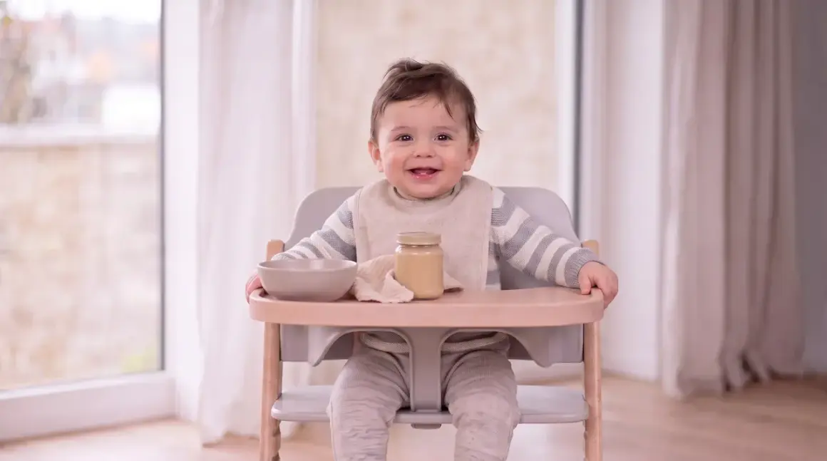 Ein lächelndes Baby sitzt im Hochstuhl, bereit für Brei. Was kann ein Baby mit 9 Monaten? Es kann schon viel, wie dieses fröhliche Kind beweist!