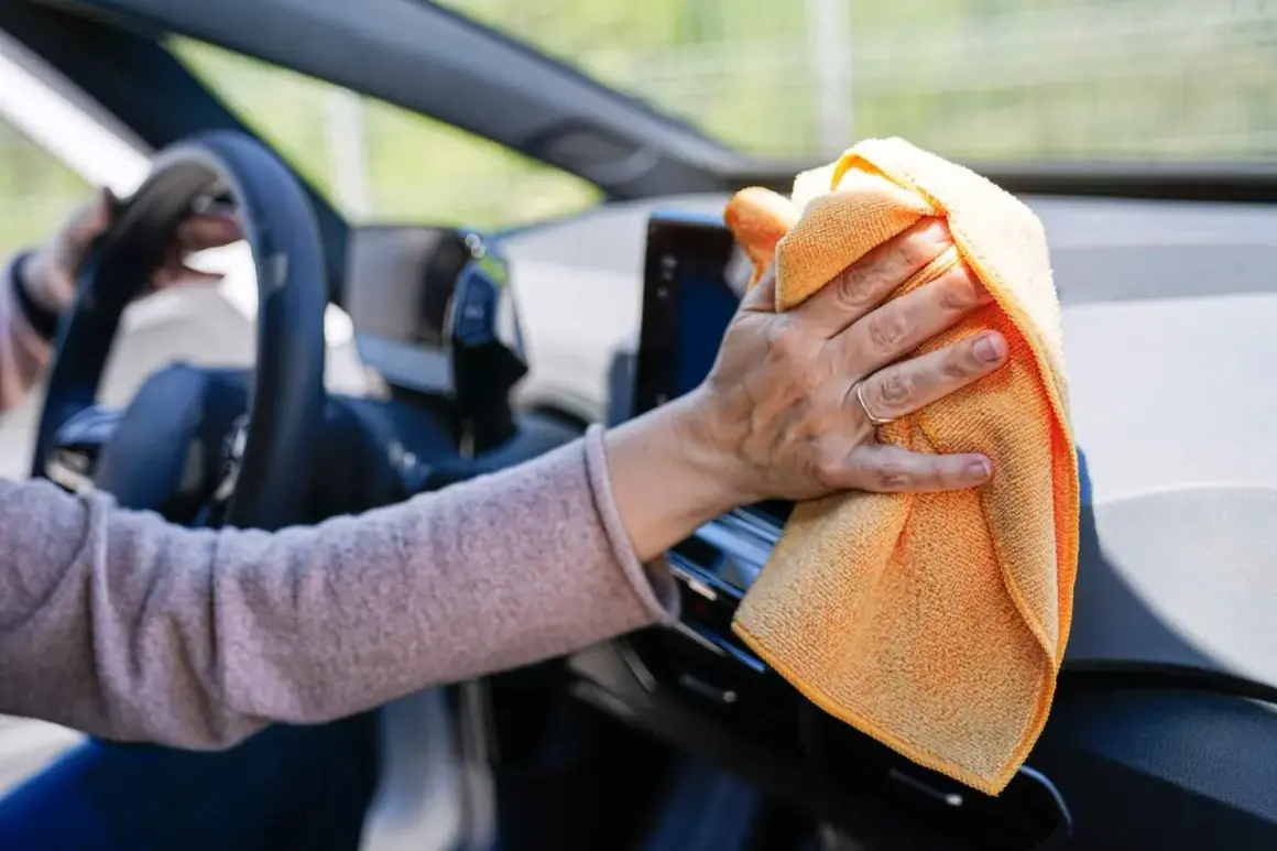 Mano limpiando el salpicadero del coche con un paño naranja. Descubre trucos caseros para limpiar el salpicadero del coche y mantenerlo impecable.