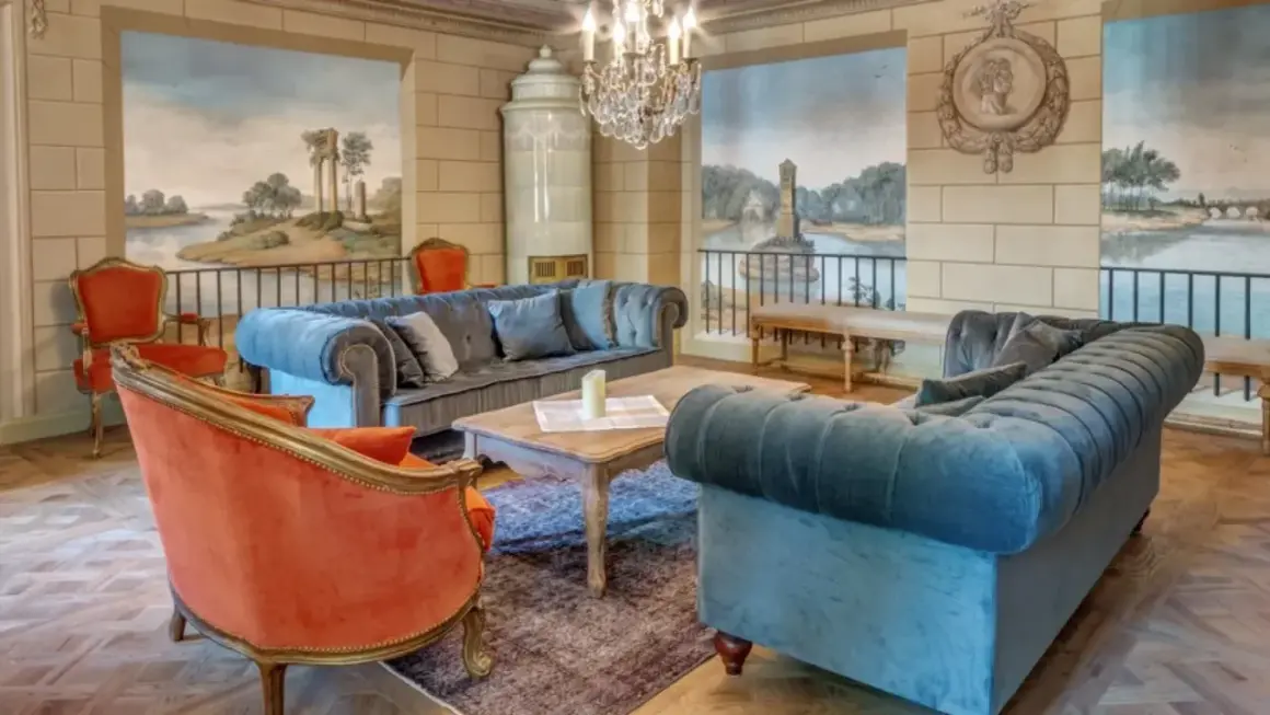 Elegancki salon w hotelu 5 gwiazdkowym. Miękkie sofy, aksamitne fotele i zabytkowy piec tworzą przytulną atmosferę.