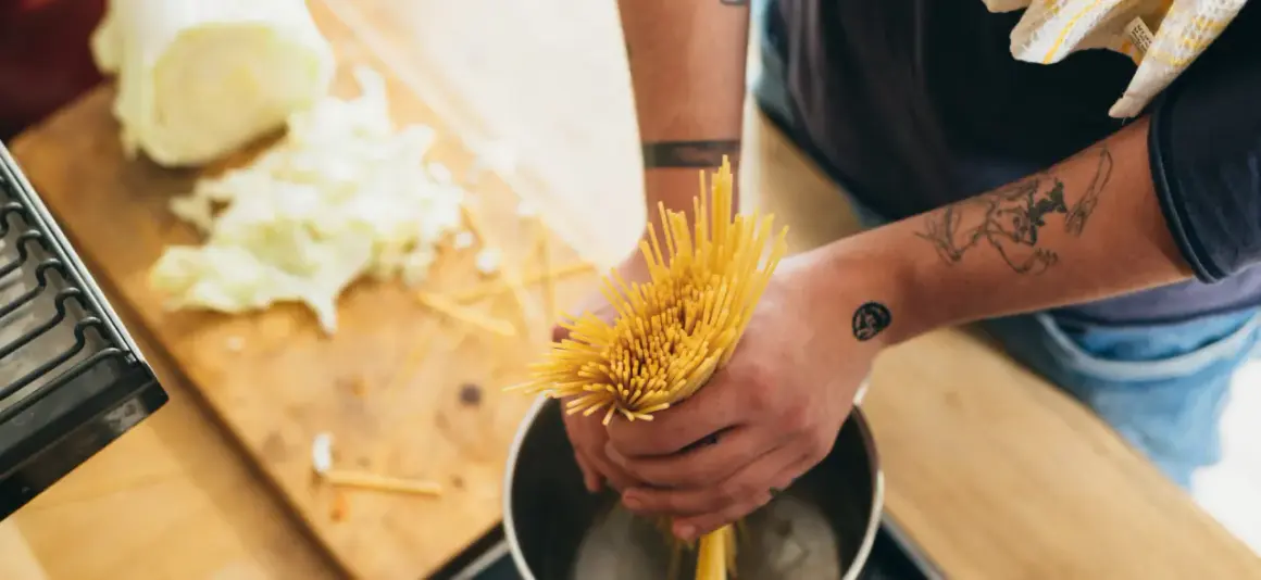 Hände mit Tattoos halten Spaghetti über einen Topf. Das bedeutet al dente: perfekt gekochte Pasta.