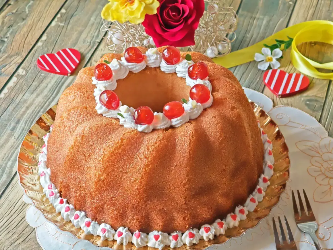 Un delicioso baba postre decorado con crema batida y cerezas rojas, listo para celebrar el amor.