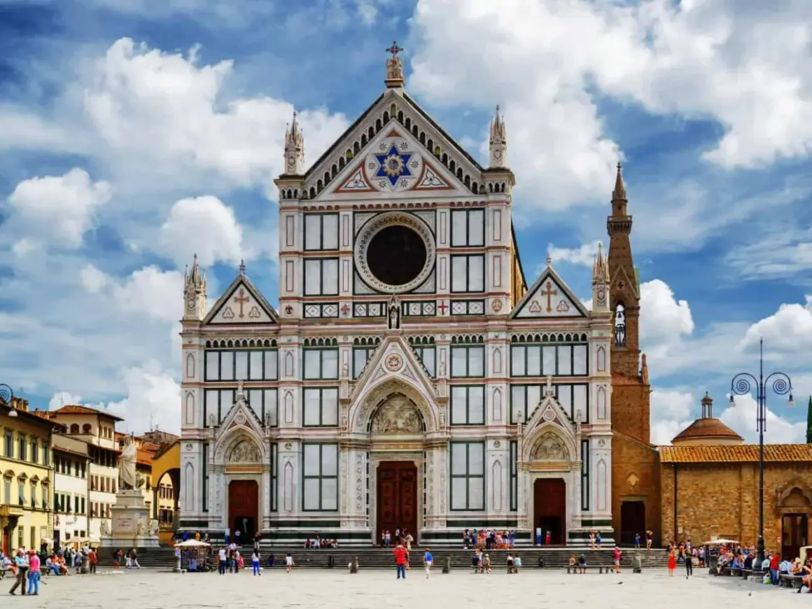 La magnifica facciata della Basilica di Santa Croce domina la piazza, con il cielo azzurro e nuvole bianche.