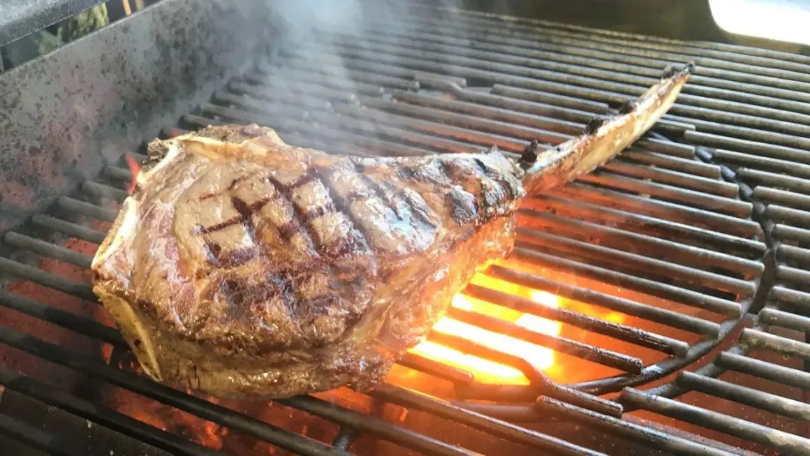 Ein saftiges Tomahawk Steak grillen, mit sichtbaren Grillstreifen und Flammen darunter.