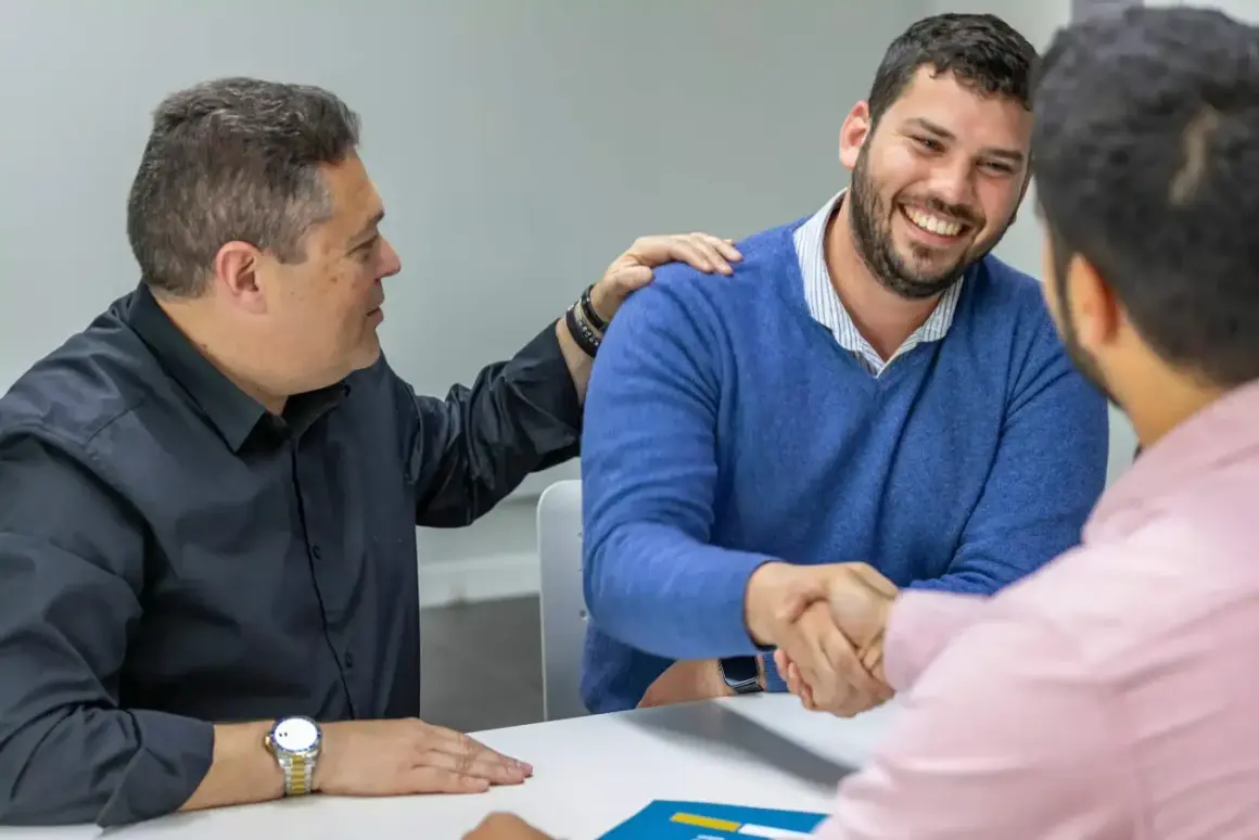 Hombres estrechando manos y sonriendo. Uno pone una mano en el hombro del otro, como si cerraran un trato importante, quizás sobre cómo es obligatorio tener seguro de hogar.