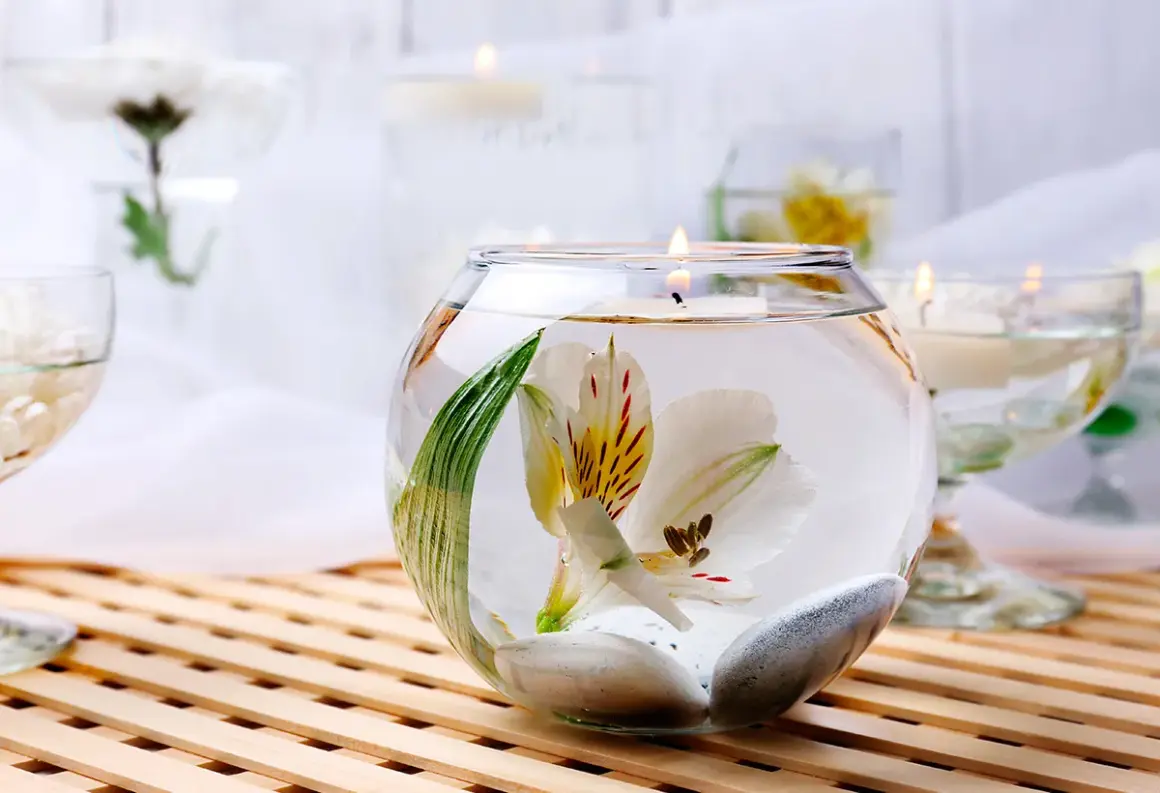 Comment décorer un grand vase en verre transparent : une fleur blanche flottant avec des galets et une bougie allumée.
