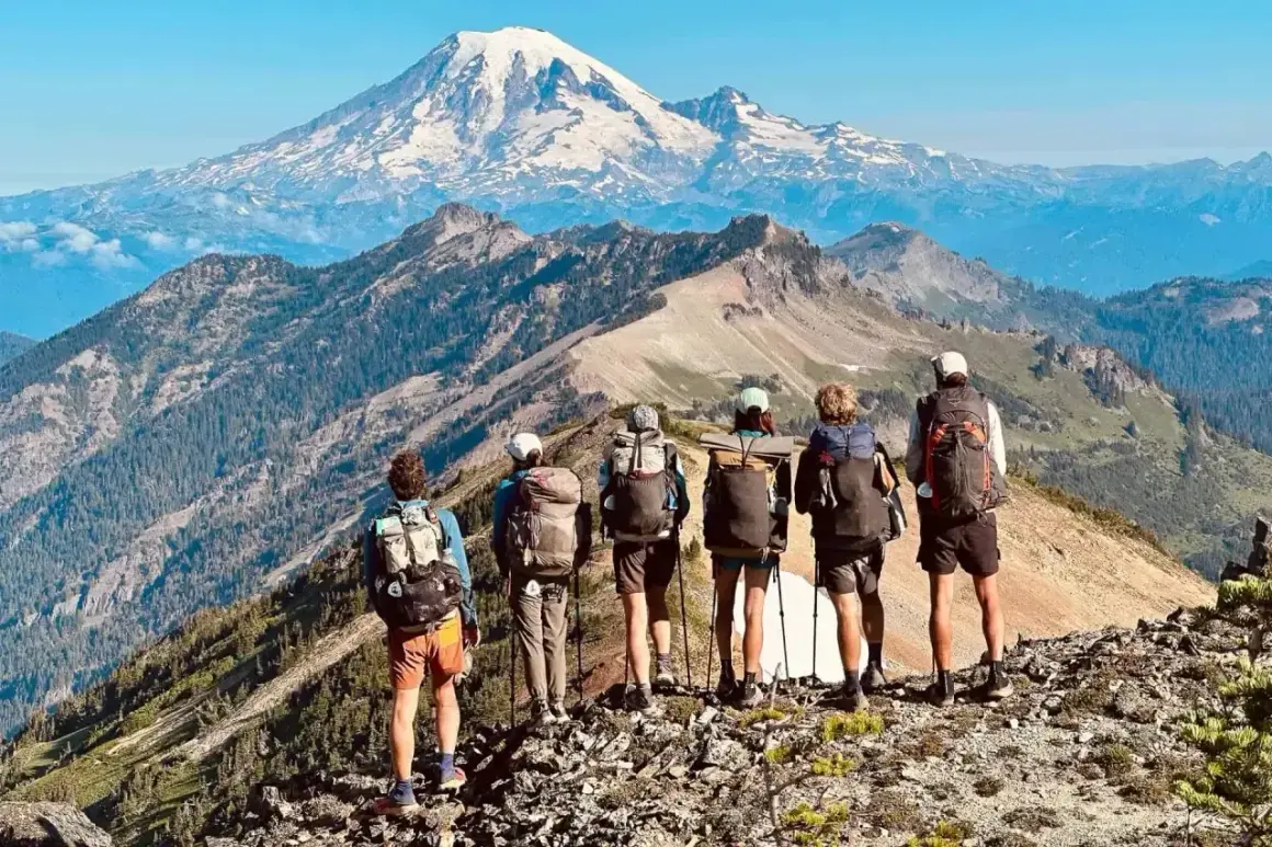 Sześcioro turystów z plecakami na grani, podziwiających majestatyczny szczyt. Przygoda na Pacific Crest Trail trwa.