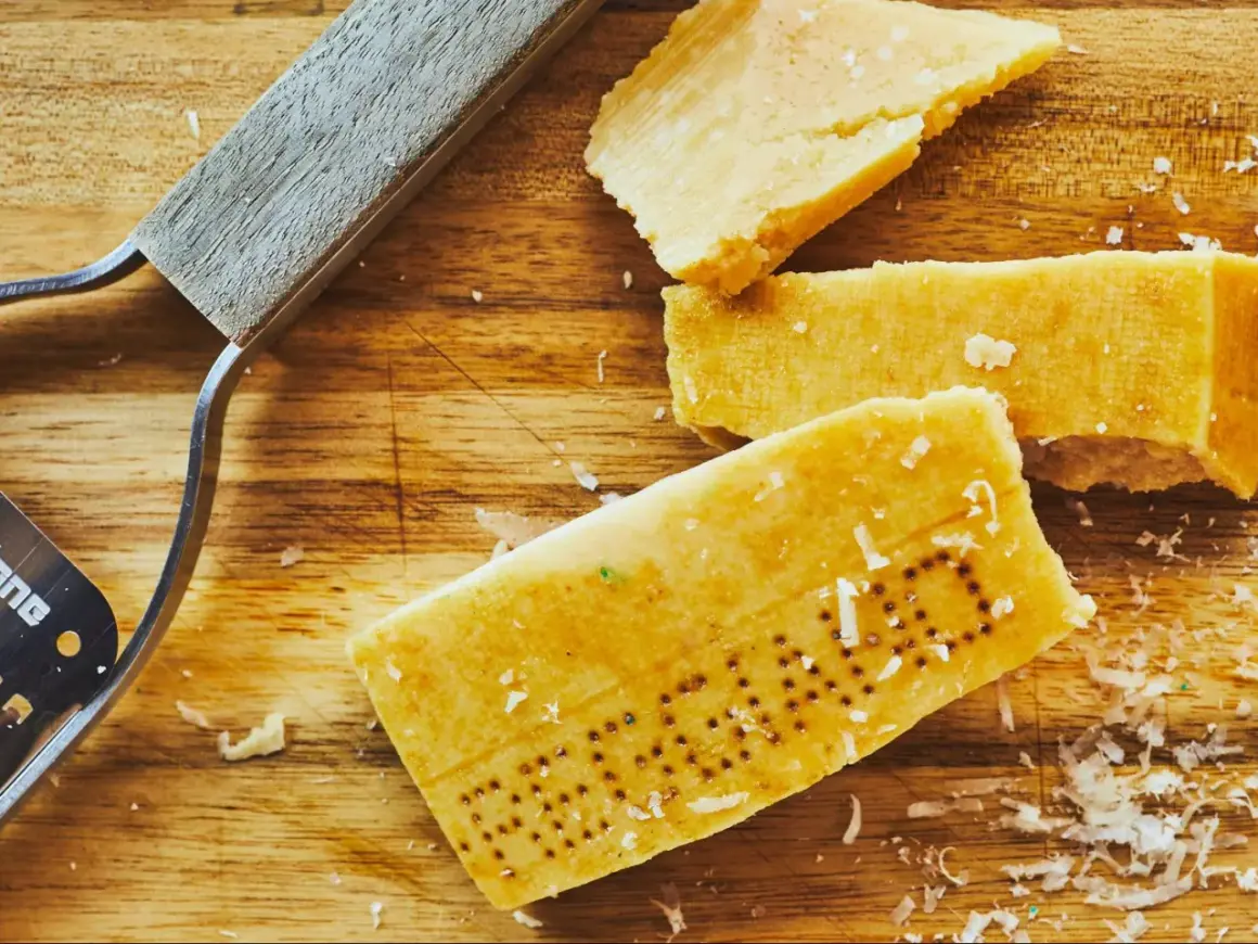 Des morceaux de **croûte parmesan comestible** sur une planche en bois, avec un râpe à fromage.