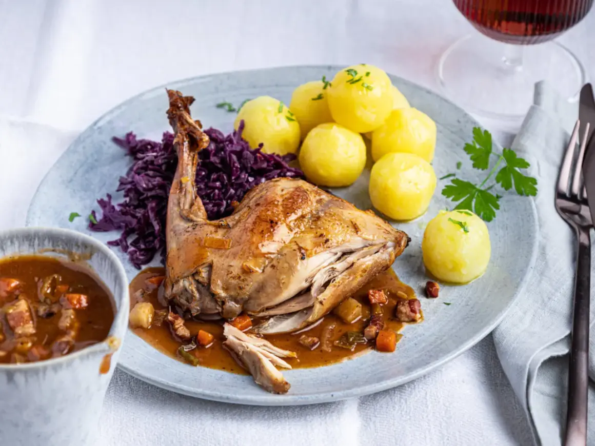 Rezept Hasenbraten im Backofen: Saftiges Kaninchen mit Klößen, Rotkohl und Sauce auf einem Teller.