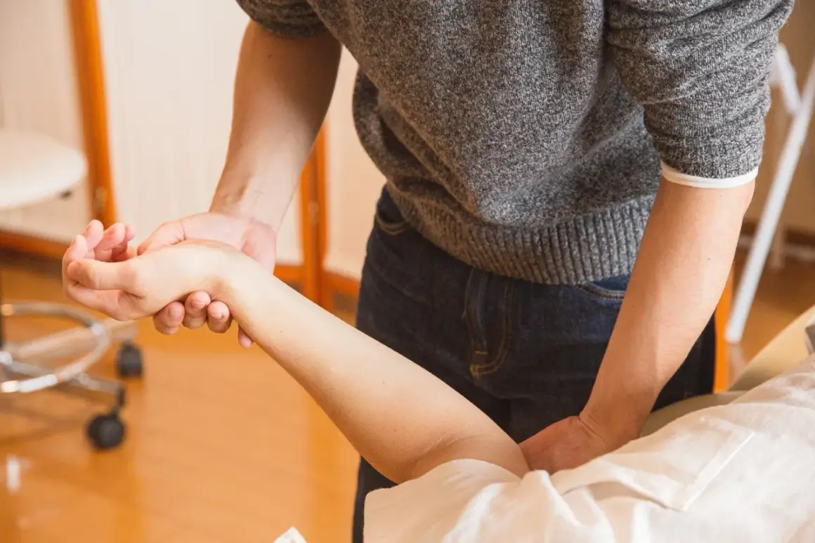 Fizjoterapeuta pomaga pacjentowi w ćwiczeniach po zabiegu cieśni nadgarstka, delikatnie masując przedramię.