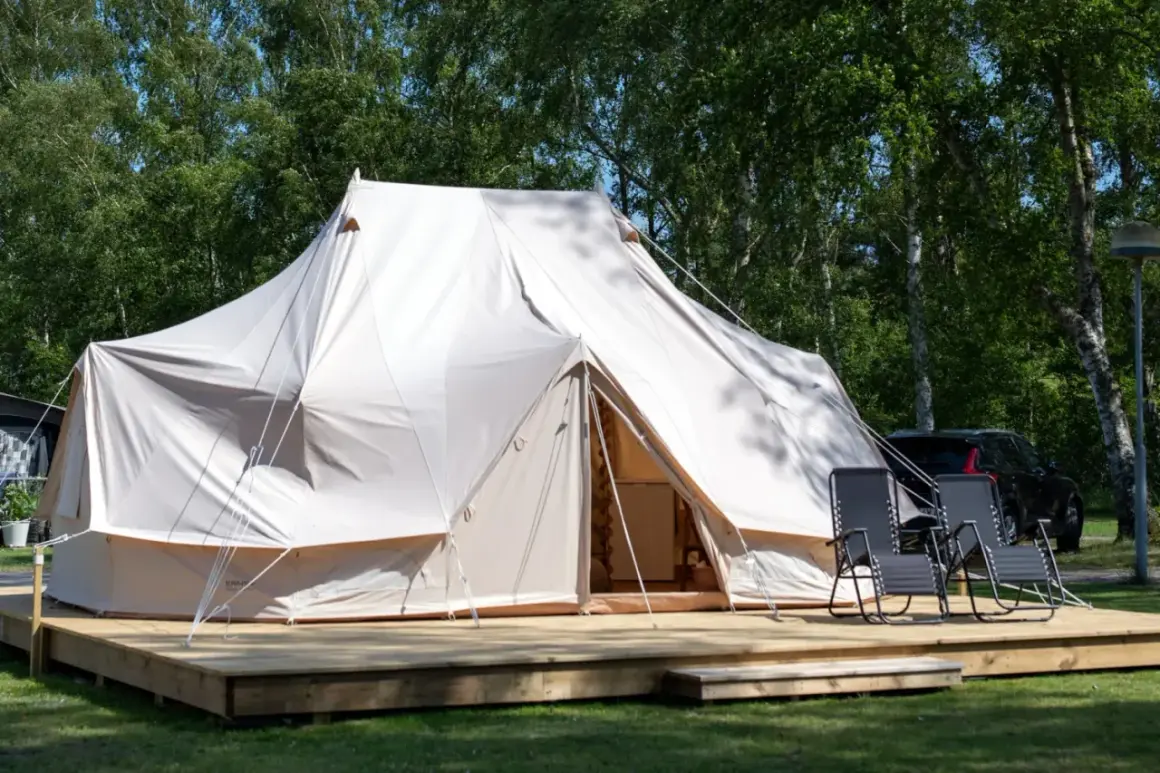 Stor glampingtält i Mölle med träaltan och solstolar. En bil syns i bakgrunden.