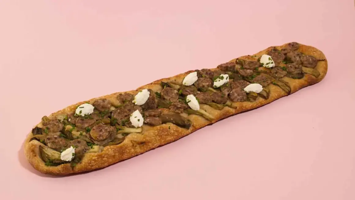 Deliciosa coca de recapte con salchicha, alcachofas y queso de cabra, lista para compartir.