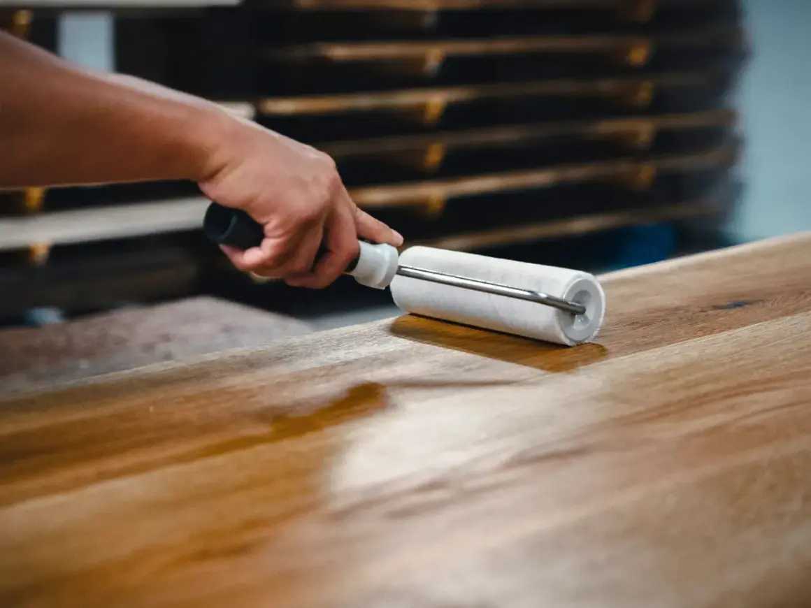 Main d'artisan appliquant un vernis sur un plateau en bois avec un rouleau, étape clé pour savoir comment vitrifier une table en bois.
