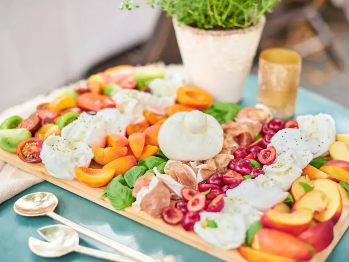 Antipasti-Platte mit Kerze, Wurst, Käse, Oliven und Brot auf Holztisch.