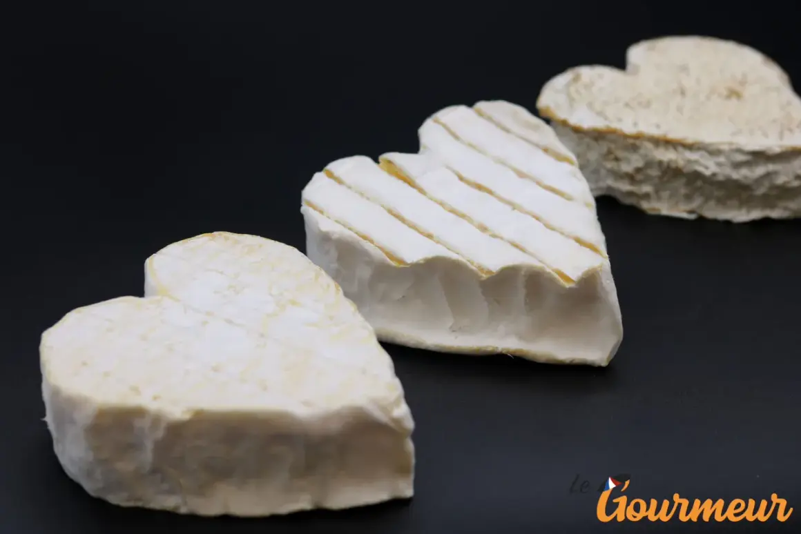 Trois fromages Neufchâtel en forme de cœur, dont un avec des stries, sur fond noir.