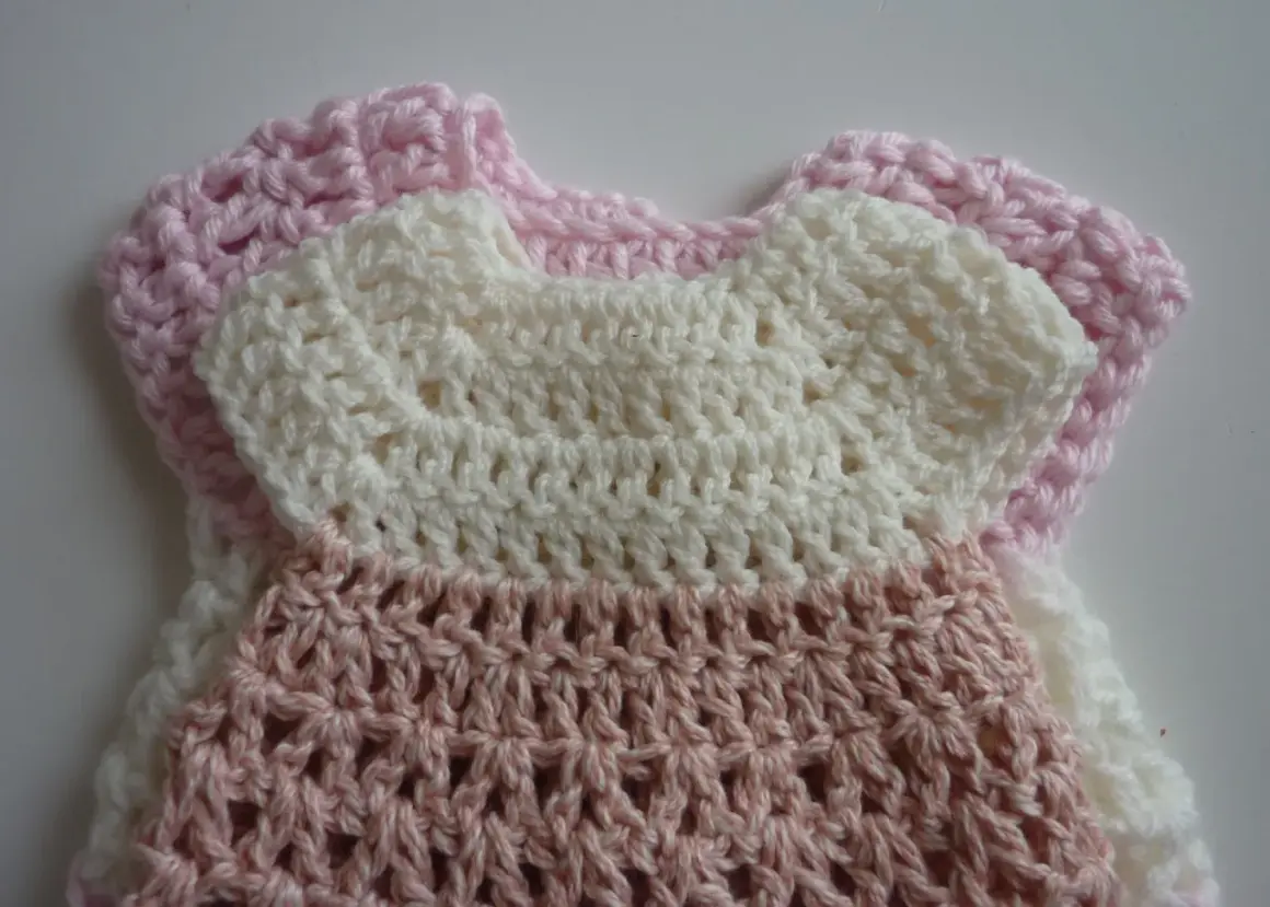 Crocheted baby dress in pink and white with openwork pattern.